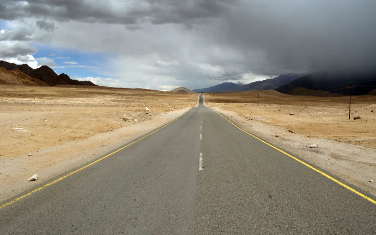 An open road through Ladakh’s high desert under storm clouds